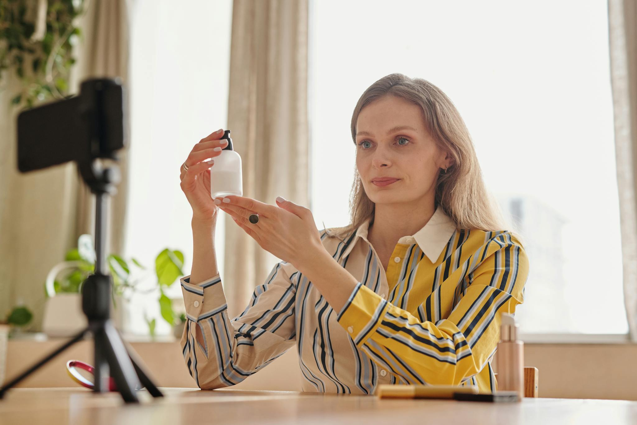 Woman demonstrates skincare product during a vlog in a cozy indoor setting.